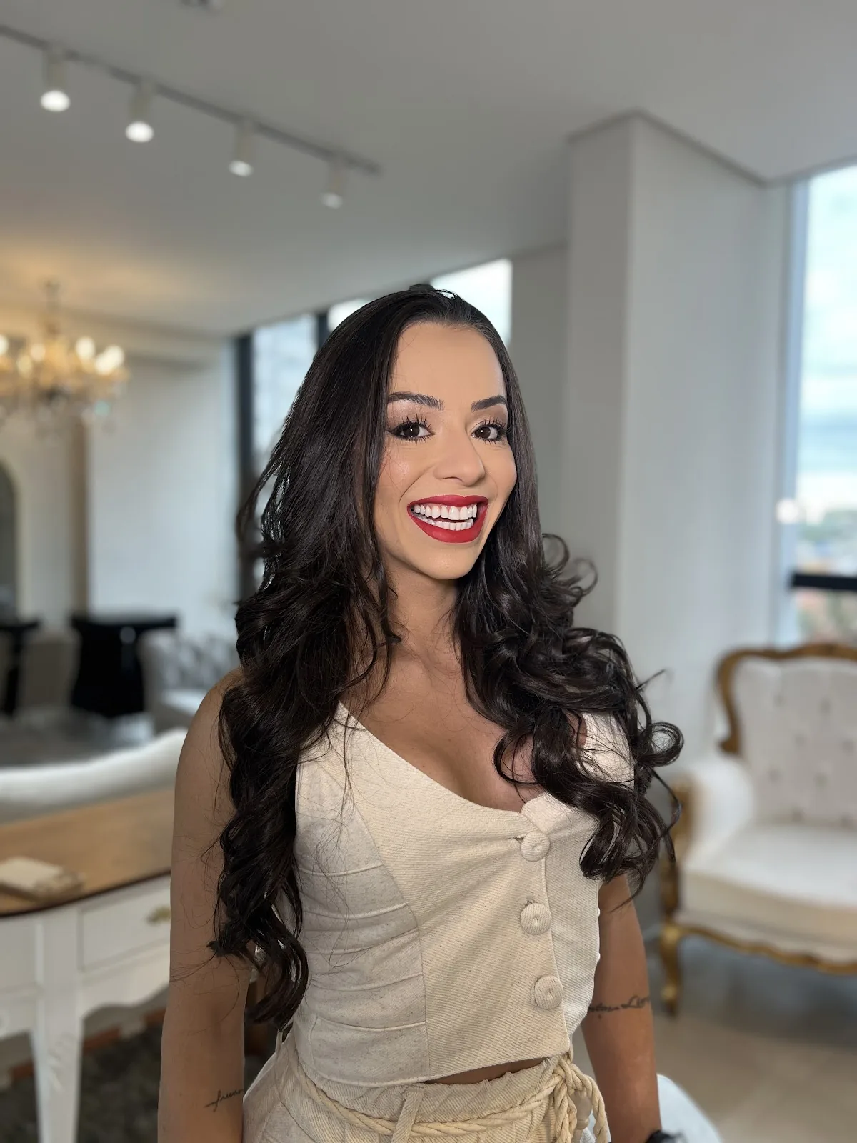 Larissa Melo sorrindo, de blusa creme, num ambiente claro com lustre